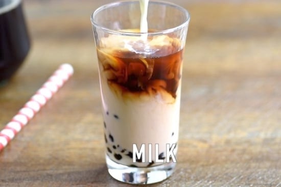 Milk being poured into glass with tea and boba