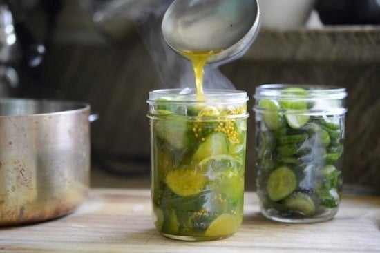 Pouring brine over cucumber and onion slices in canning jars