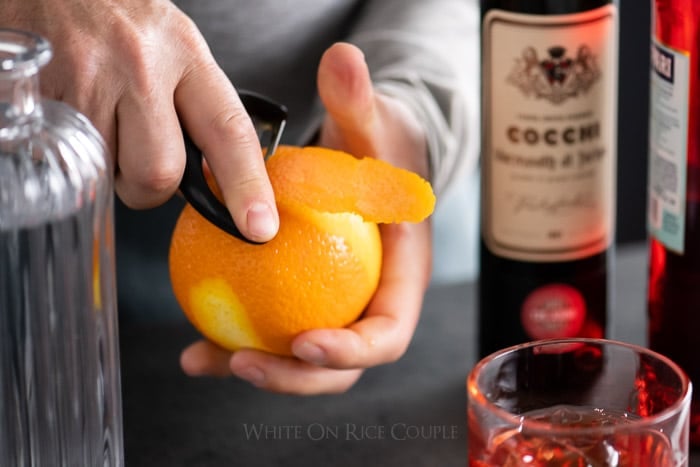 Peeling an orange for the garnish on a negroni cocktail recipe from whiteonricecouple.com