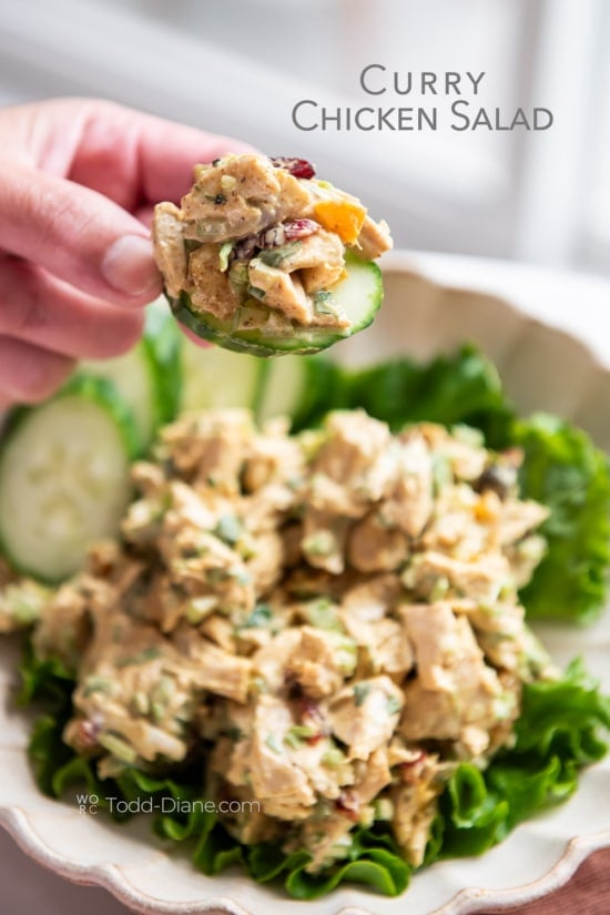hand holding a cucumber topped with curry chicken salad 