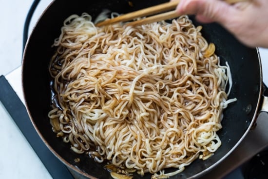 Noodles being tossed with sauce in pan