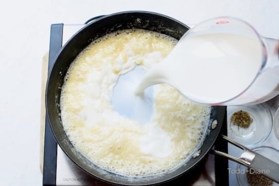 Milk being poured into skillet with butter, garlic, and flour