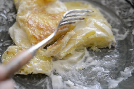 Cutting into a piece of potatoes au gratin with a fork