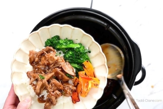 Spooning slow cooker teriyaki chicken onto a bowl with rice and veggies