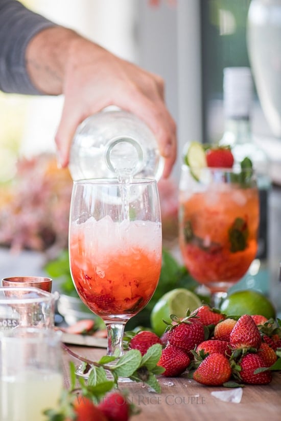 pouring sparkling water into strawberry mojito cocktail