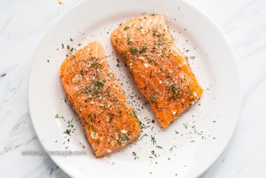 Salmon fillets coated with salt, pepper, garlic, and herbs on a plate