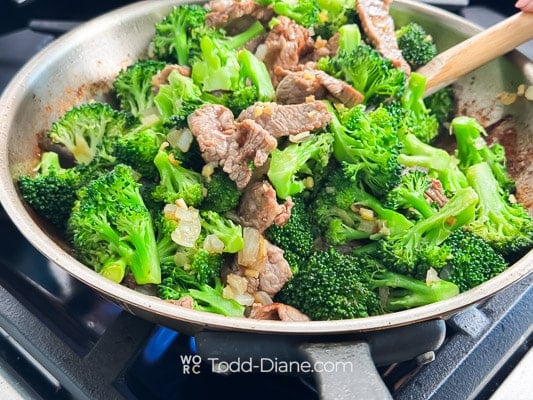 adding broccoli to the beef pan