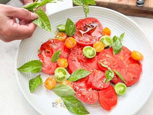 adding fresh torn basil on tomato salad