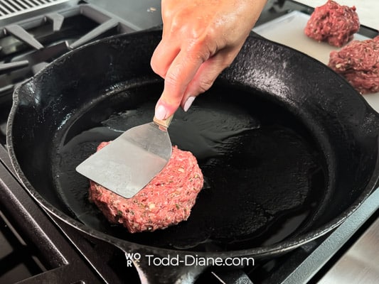smashing lamb burger patty on skillet