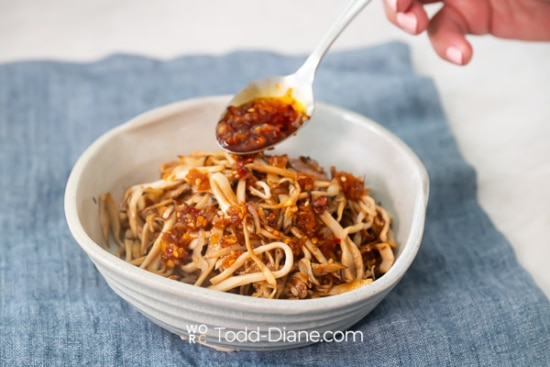 adding chili crunch over mushroom noodles