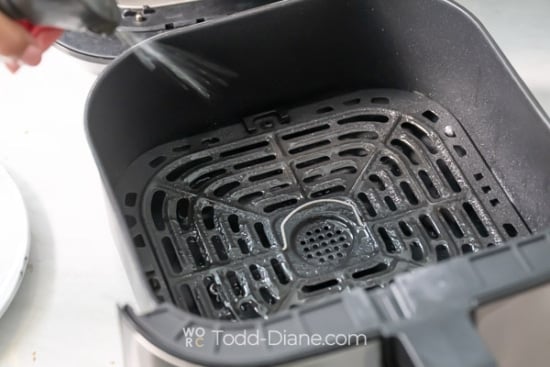 Spraying air fryer basket with oil