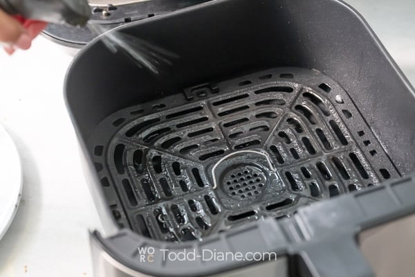 Spraying air fryer basket with oil