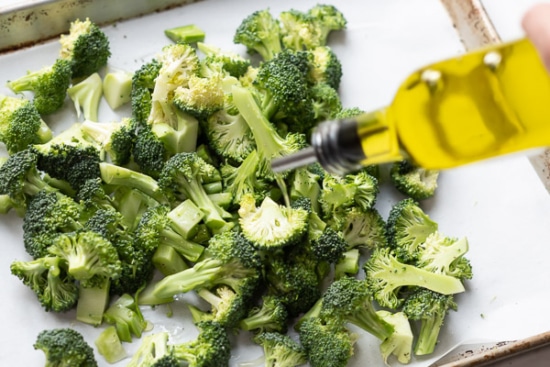 Oiling broccoli on parchment paper lined sheet pan