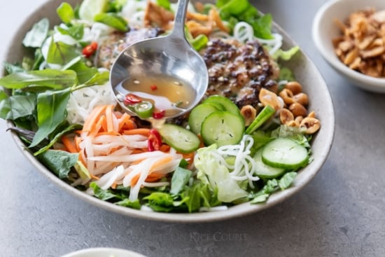 drizzling fish sauce over noodle bowl