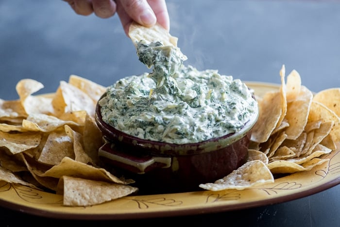 stove top Artichoke Spinach Dip hand dipping chip into dip