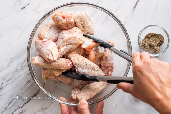 Turning raw chicken wings in a bowl with salt and pepper