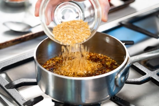 Dried garlic being poured into pan with cooked garlic